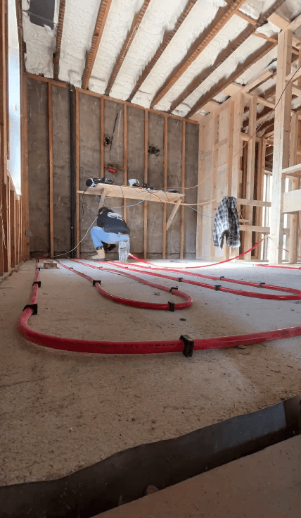Red radiant heating pipes installed on a concrete floor in an unfinished wood-framed room.